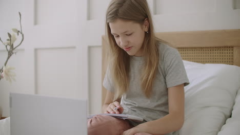 Teenager-Mädchen-Bereitet-Sich-Auf-Den-Online-Unterricht-über-Das-Internet-Vor-Und-Hält-Ein-Schreibheft-Auf-Dem-Bett-Vor-Dem-Laptop